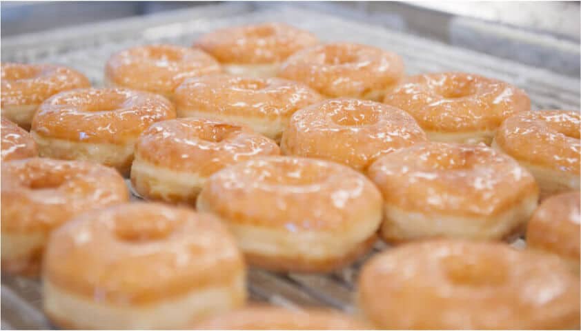 A tray of freshly glazed doughnuts from your favorite QSR franchise cools on a metal rack, inviting you to indulge in their sweet perfection.